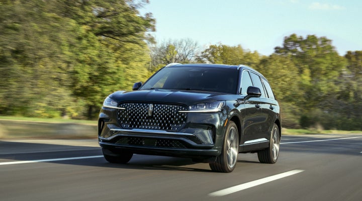 A 2026 Lincoln Black Label™ Aviator® SUV is being driven down a road lined with trees. | Hines Park Lincoln in Plymouth MI