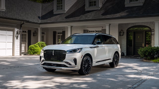 A white 2026 Lincoln Aviator® SUV is parked in the driveway of a luxury home. | Hines Park Lincoln in Plymouth MI