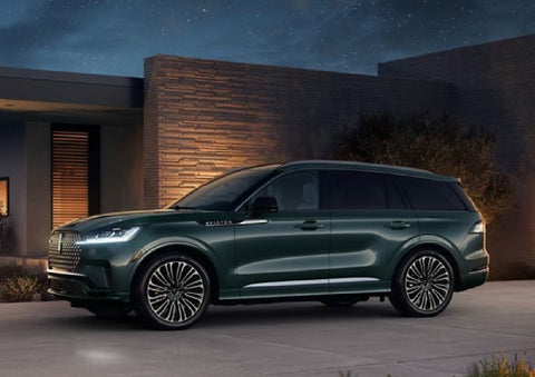 A green 2027 Lincoln Aviator® SUV is parked outside a contemporary home. | Hines Park Lincoln in Plymouth MI