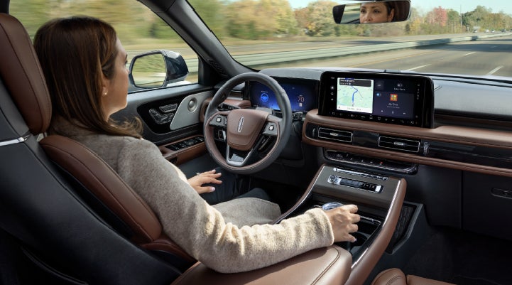 A 2027 Lincoln Aviator® SUV is being driven hands-free on a highway lined with trees. | Hines Park Lincoln in Plymouth MI