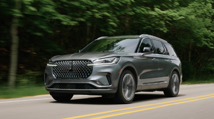 A 2027 Lincoln Aviator® SUV is being driven down a road lined with trees. | Hines Park Lincoln in Plymouth MI