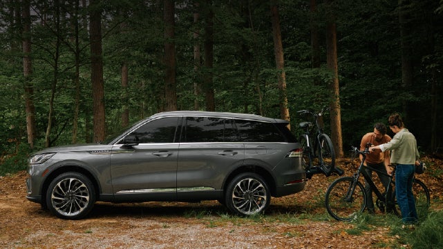A father and son load e-bikes on a bike rack attached to a 2027 Lincoln Aviator® SUV. | Hines Park Lincoln in Plymouth MI